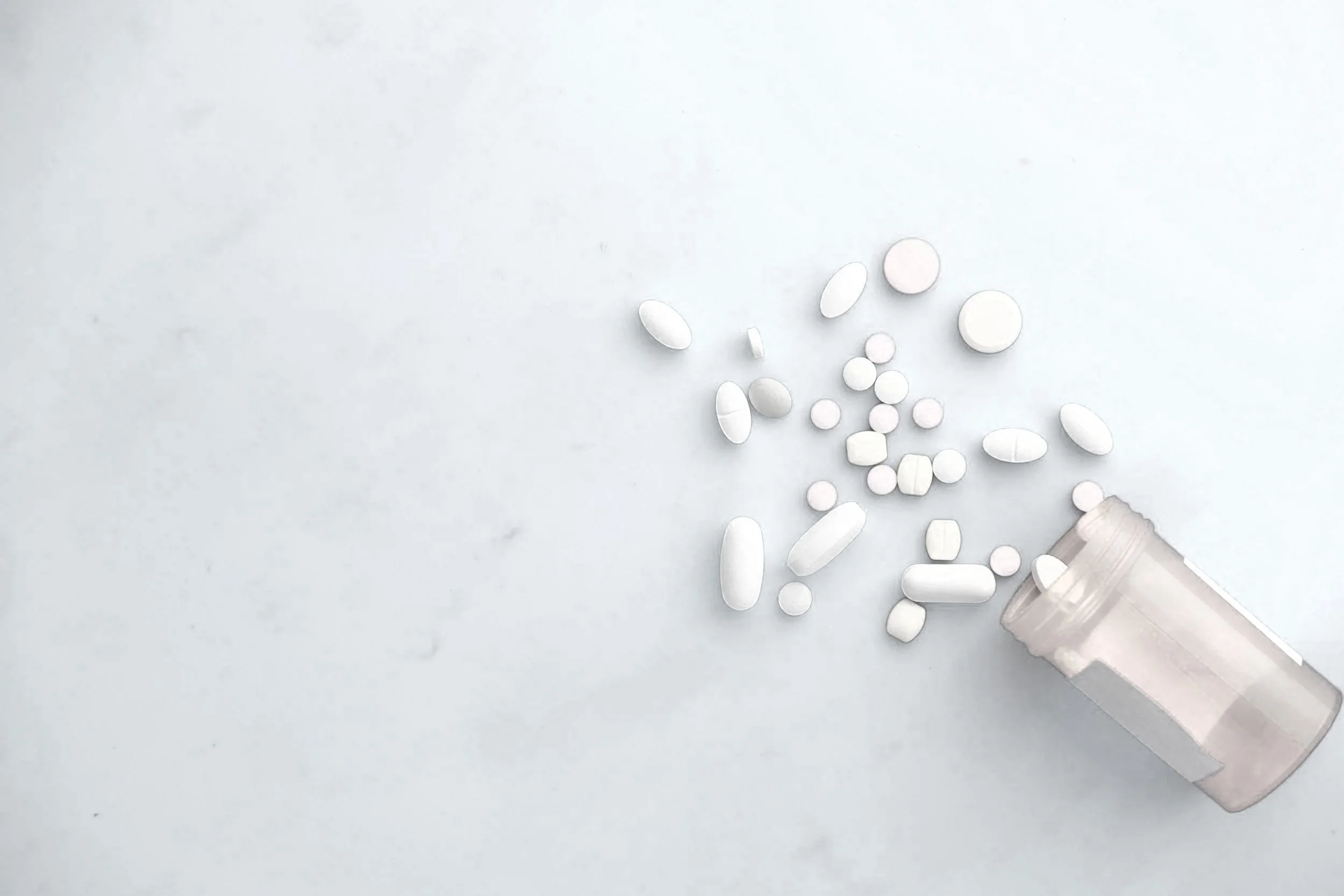 White pills spilling out from an open plastic bottle onto a white surface.