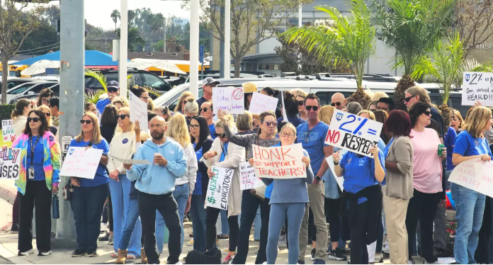 Group of people protesting with signs in a parking lot.