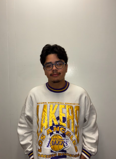 A young woman with long dark hair smiling and making peace signs with both hands inside a bus, with plush sheep stuffed animal on the window ledge next to her.