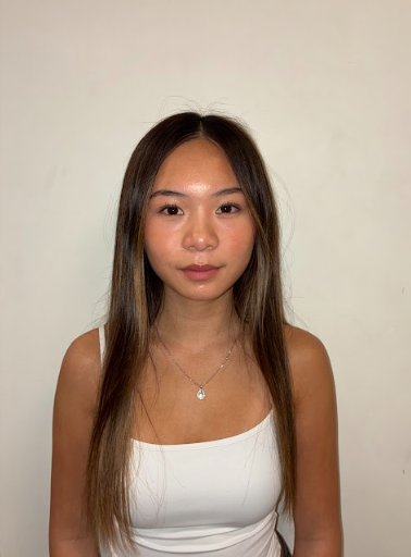 A young man with curly hair and a light complexion smiling, standing against a plain light-colored wall, wearing a hoodie.