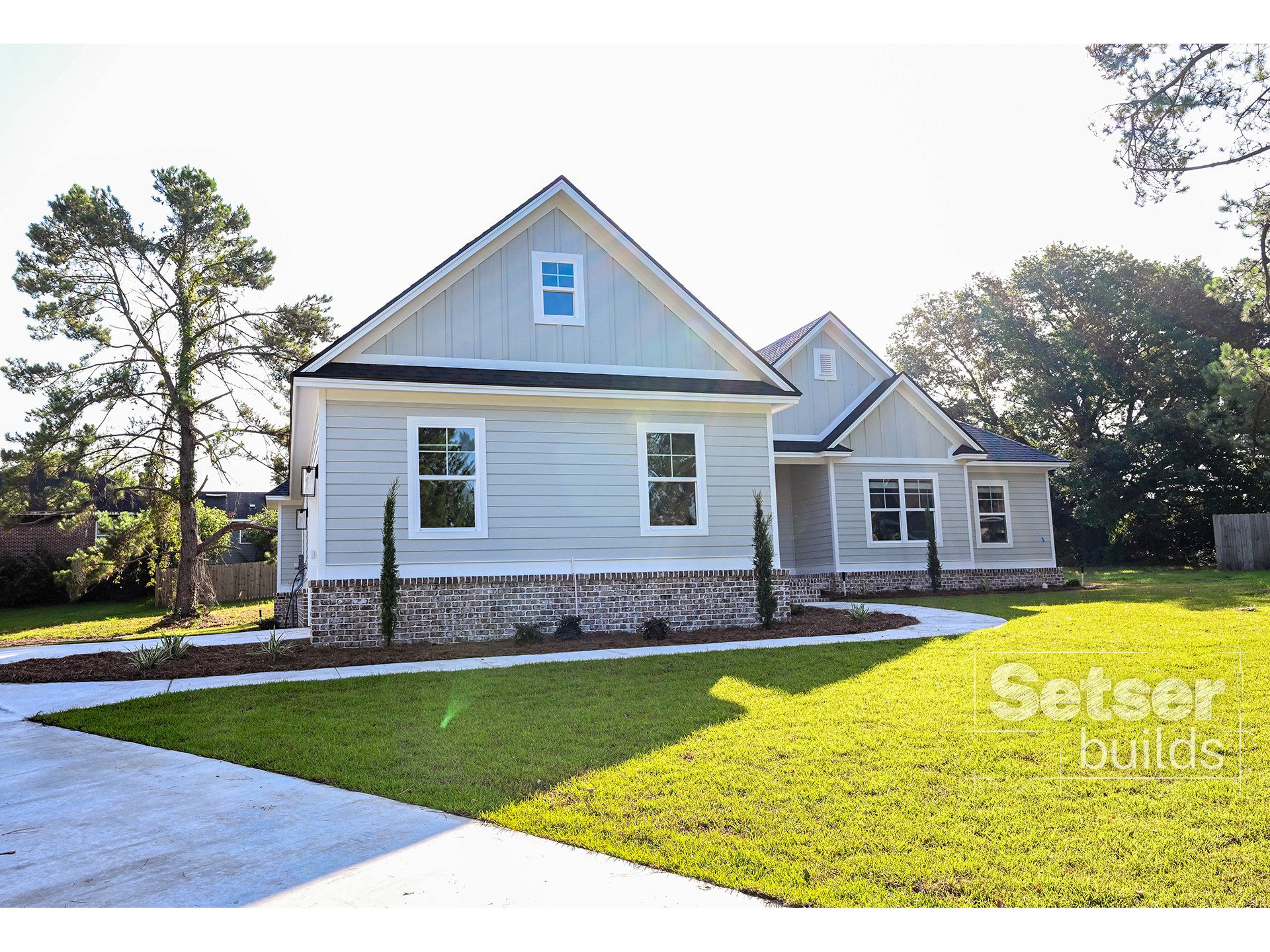 Newly built modern house with a front lawn and a concrete driveway, surrounded by trees and a clear sky.