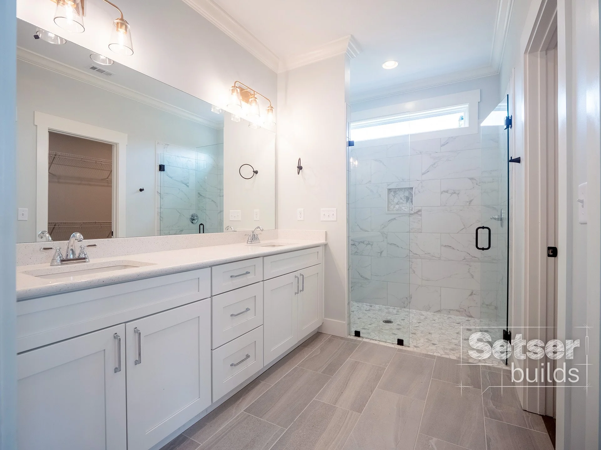 Modern bathroom with dual sinks, large mirror, and a walk-in shower with glass doors and marble tiles.