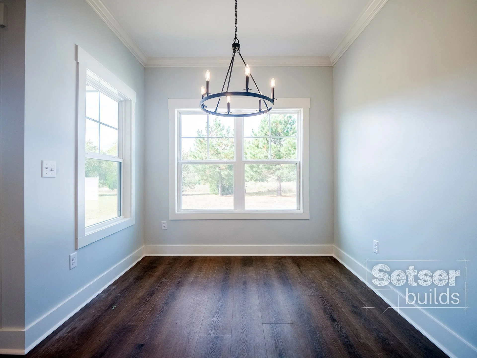Empty dining room with hardwood floors, large windows, white trim, and a modern black chandelier.