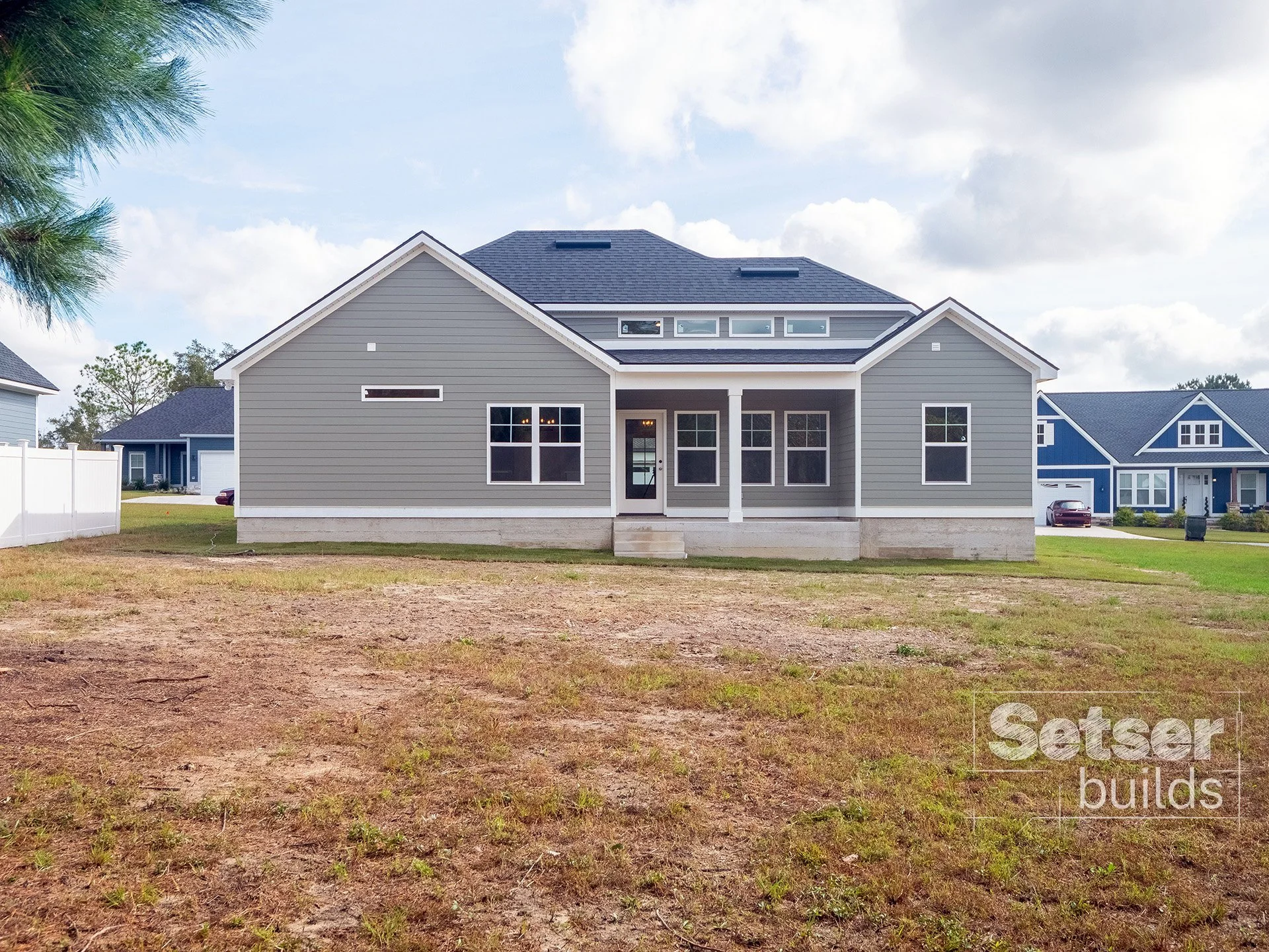 New gray house with a small front porch, multiple windows, and a dark shingle roof, located in a suburban neighborhood
