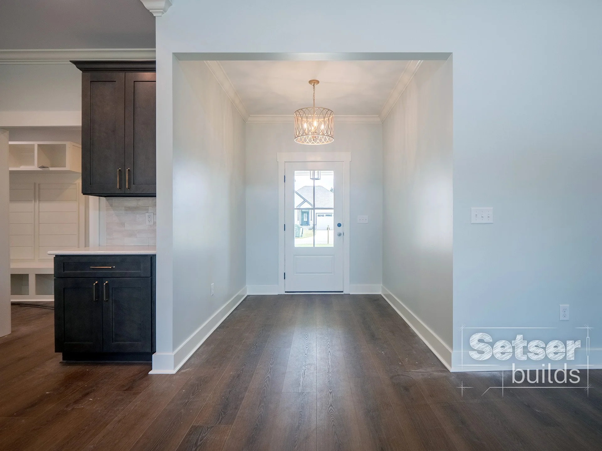 Empty dining area with hardwood floors, white walls, a hanging light fixture, and a door leading outside.