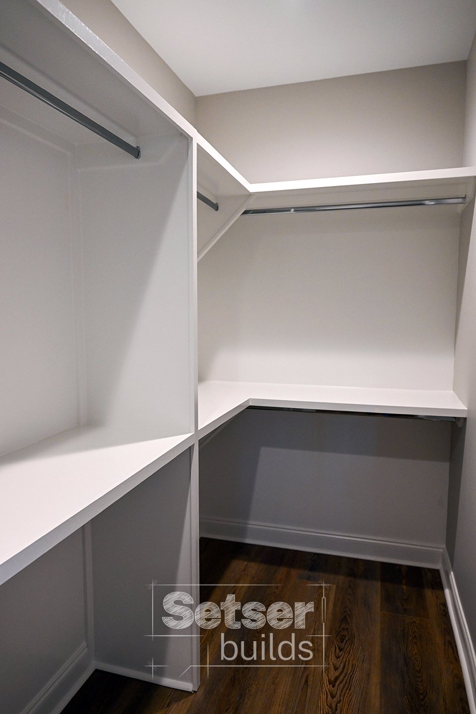 Empty white walk-in closet with multiple shelves and hanging rods, dark wood floor.