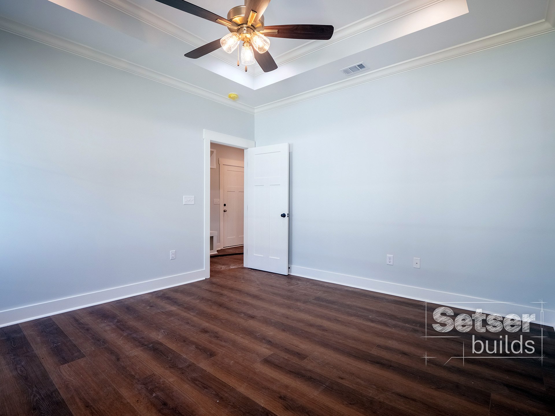 Empty room with light blue walls, a ceiling fan with lights, hardwood floors, and an open door leading to a hallway.