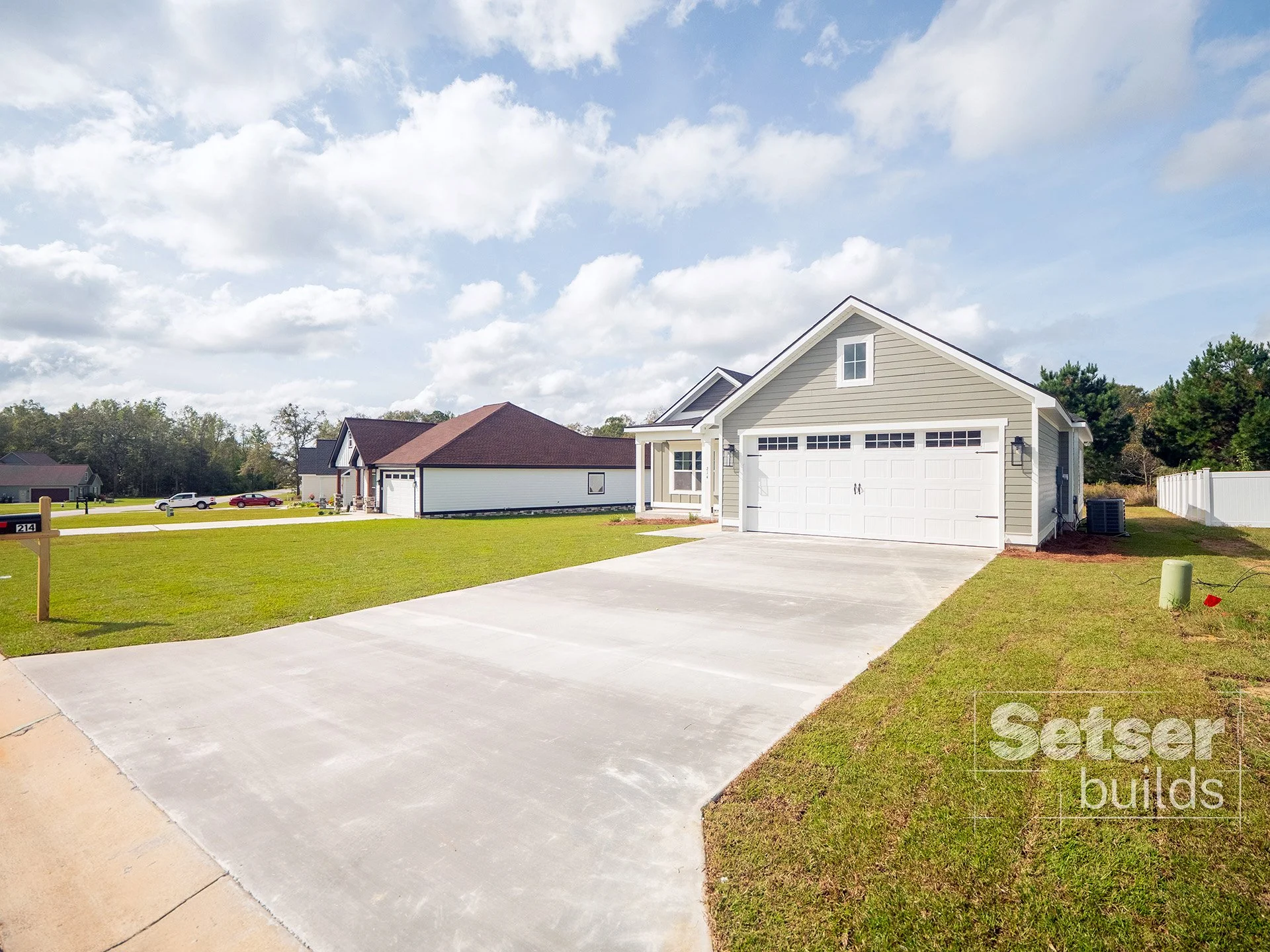Front view of a new house with a white two-car garage, grey siding, and a well-maintained front yard under a partly cloudy sky.