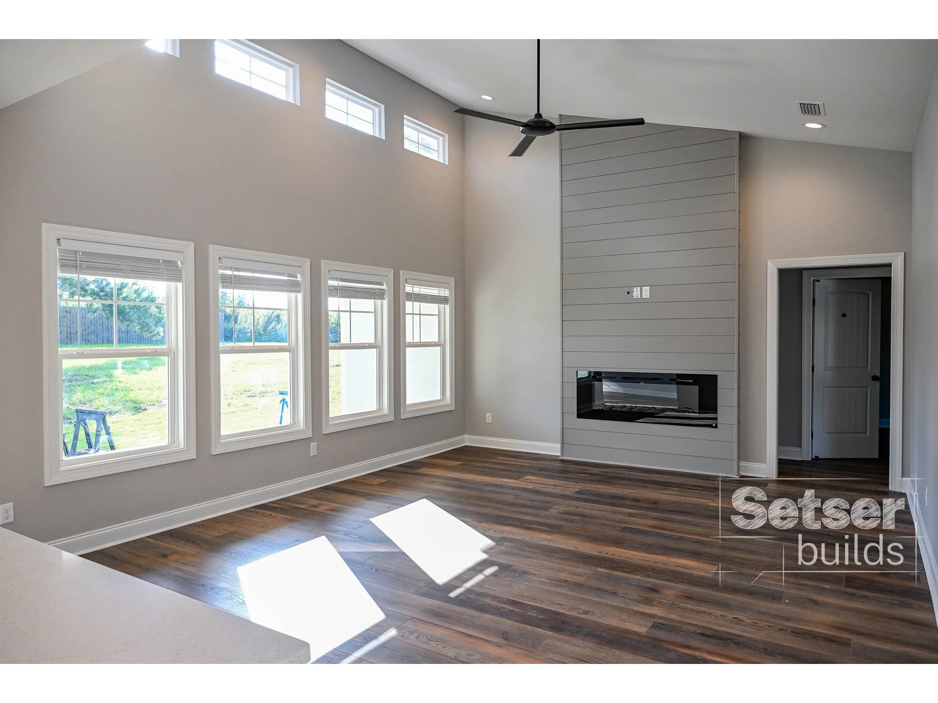 Empty living room with hardwood floors, large windows, a modern fireplace, and a ceiling fan.