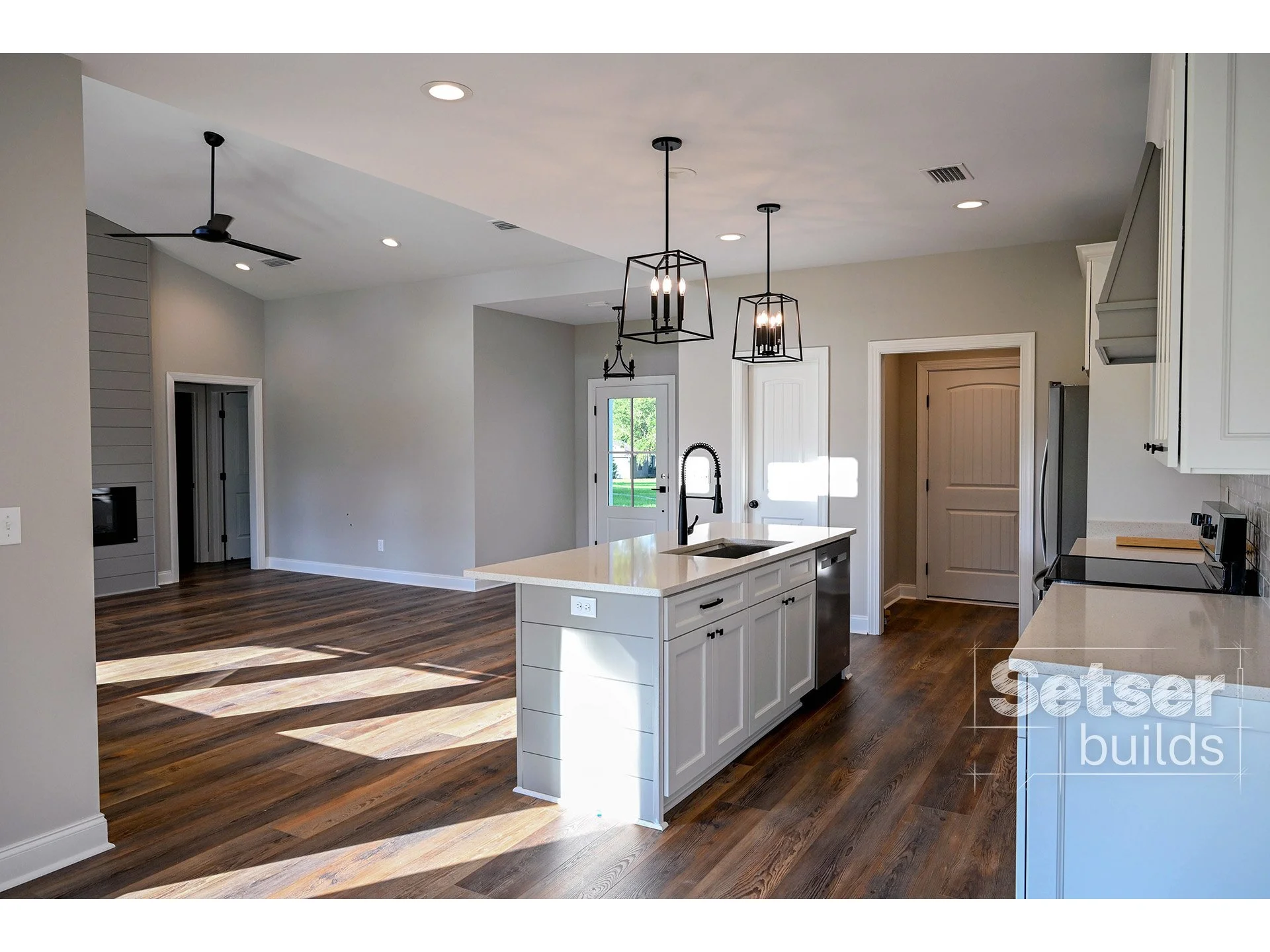 Open-concept kitchen and living area with white cabinetry, an island with a sink, pendant lighting, and hardwood floors.