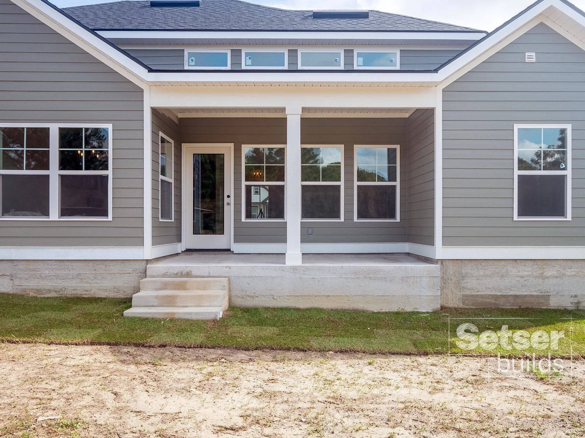 Front view of a new gray house with a covered porch, three steps leading up to it, and multiple windows. The house has a modern look with a gabled roof and white trim.