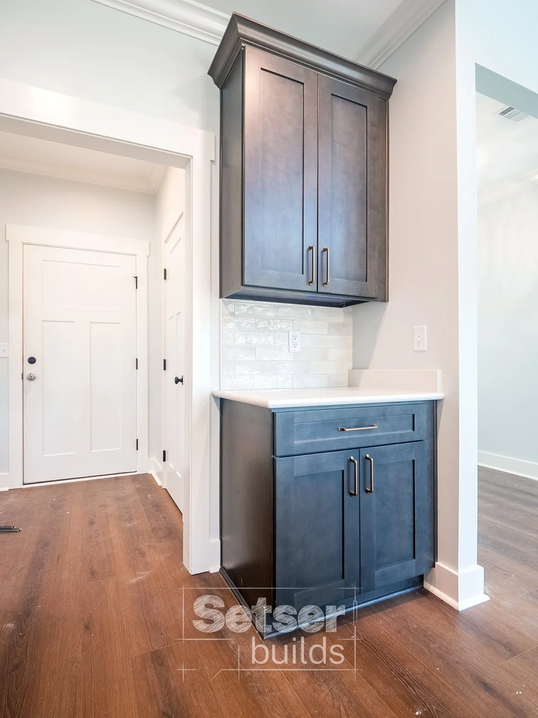 Kitchen corner with dark blue cabinets, white countertop, white subway tile backsplash, hardwood floors, and a white door.