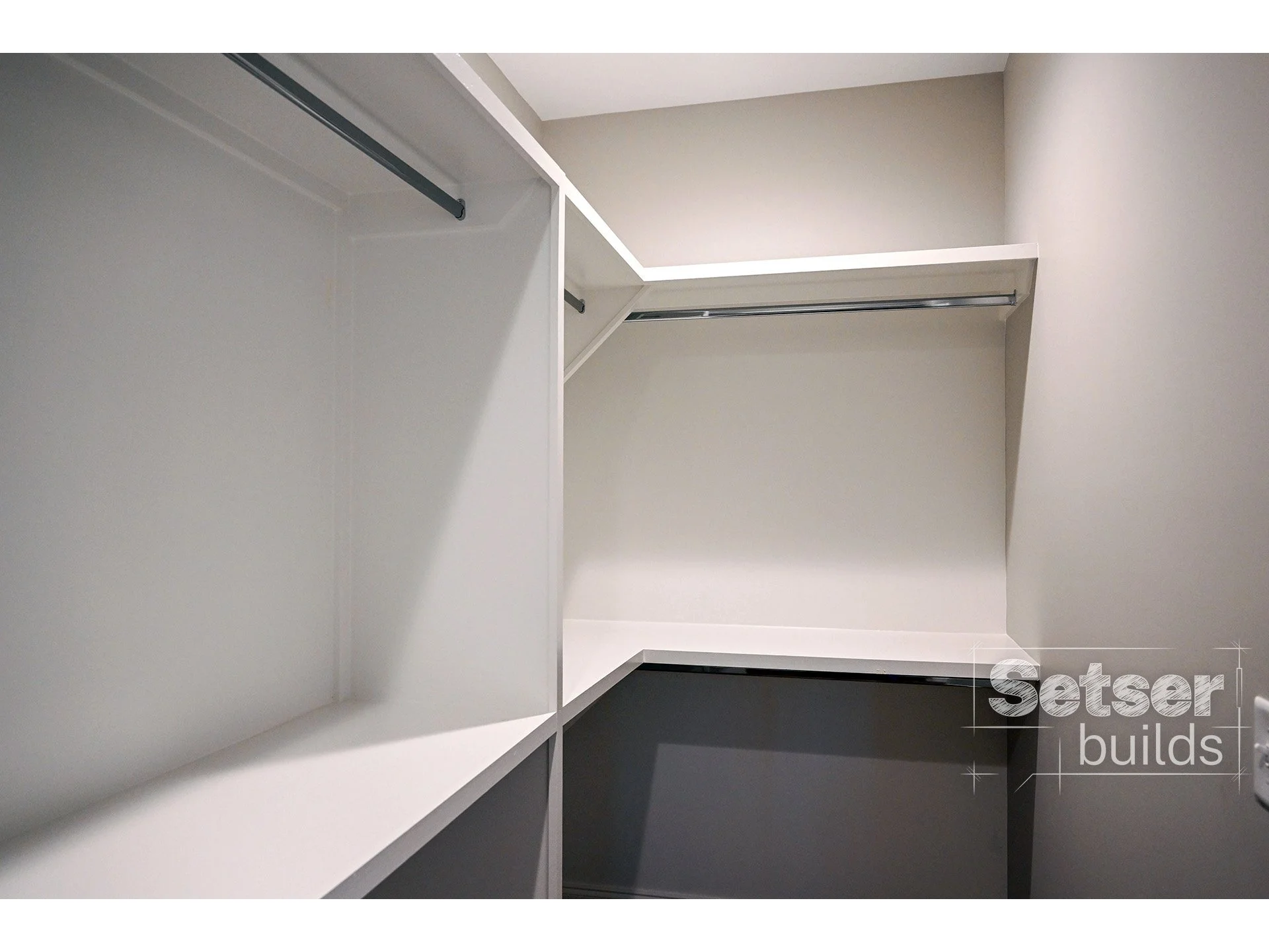 Empty white walk-in closet with shelves and hanging rods, well-lit