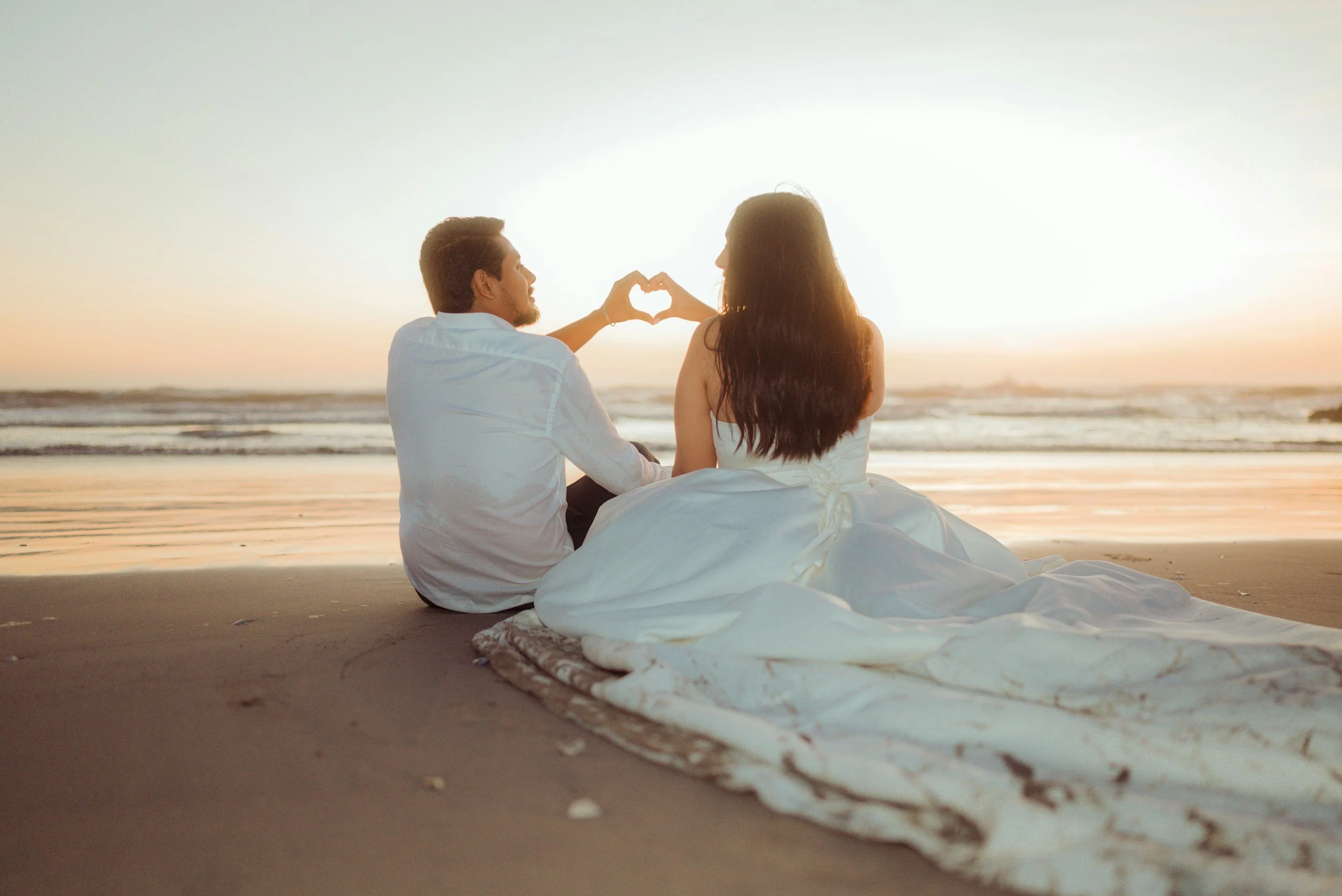 wedding couple sitting on the beach in Puerto Vallarta raising hands in the shape of a heart