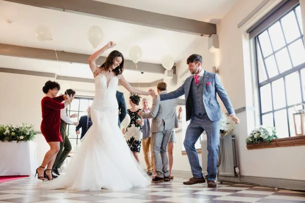 Bride and groom dancing at their wedding reception in a bright room with large windows and hanging paper lanterns.