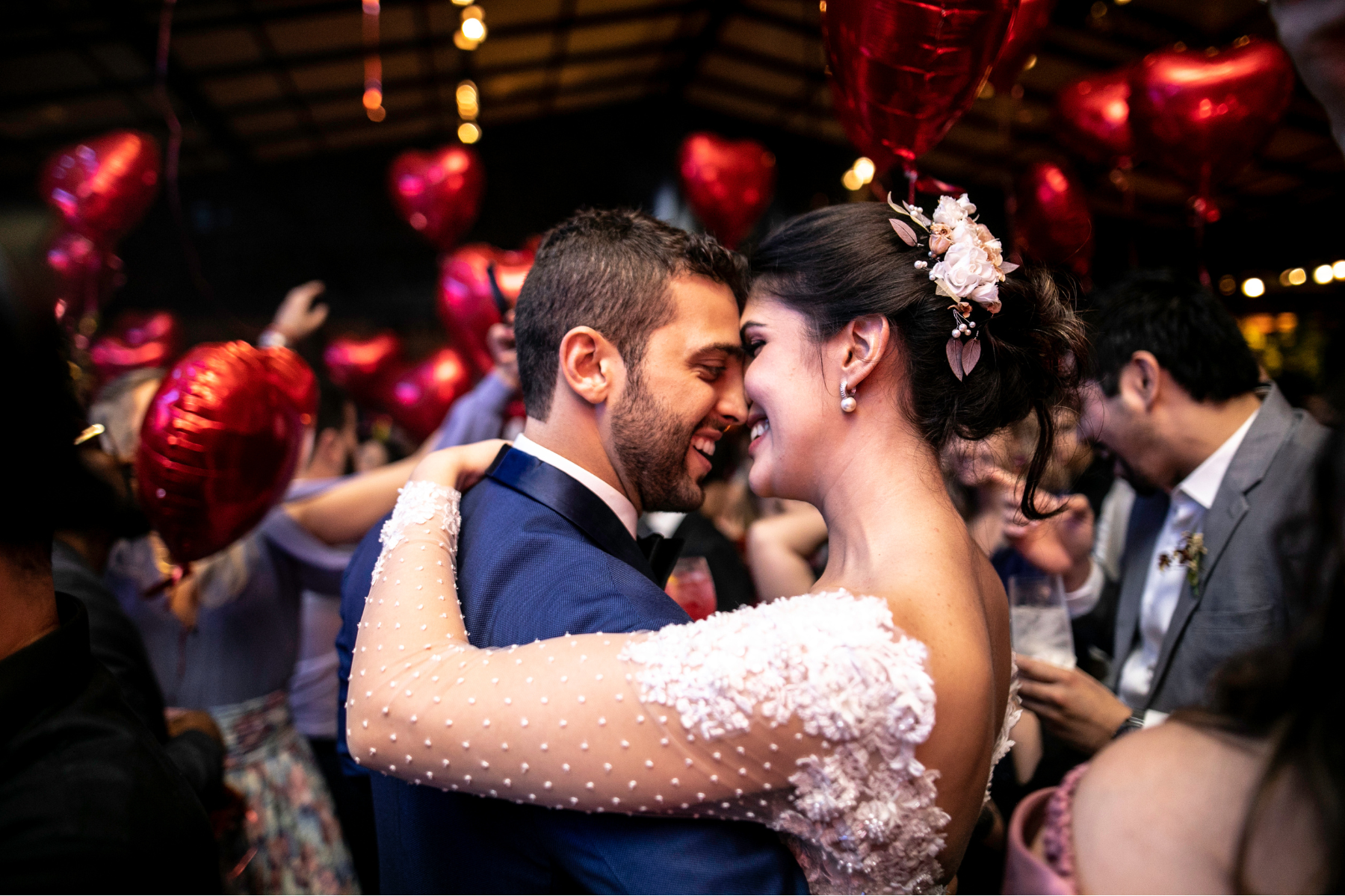 Bride and groom dancing at their wedding reception, surrounded by guests and red heart-shaped balloons.