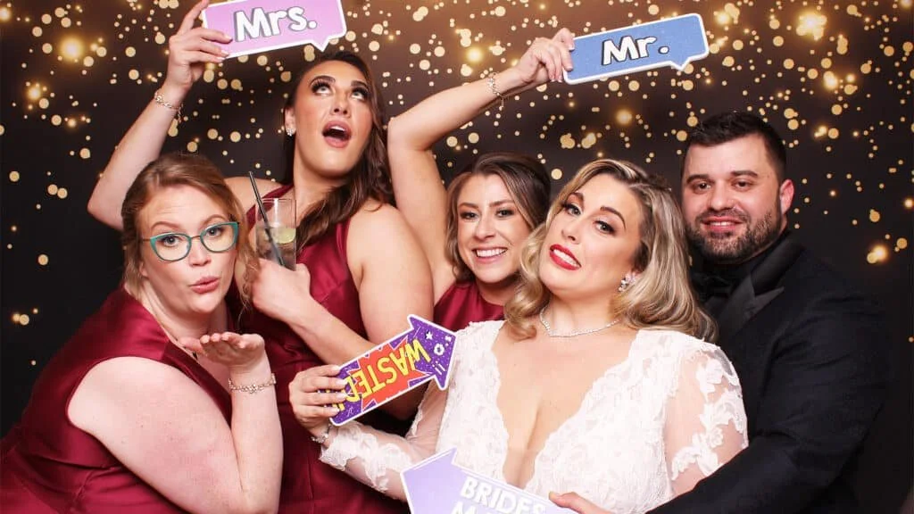 Bride and groom with three bridesmaids having fun at the photo booth.