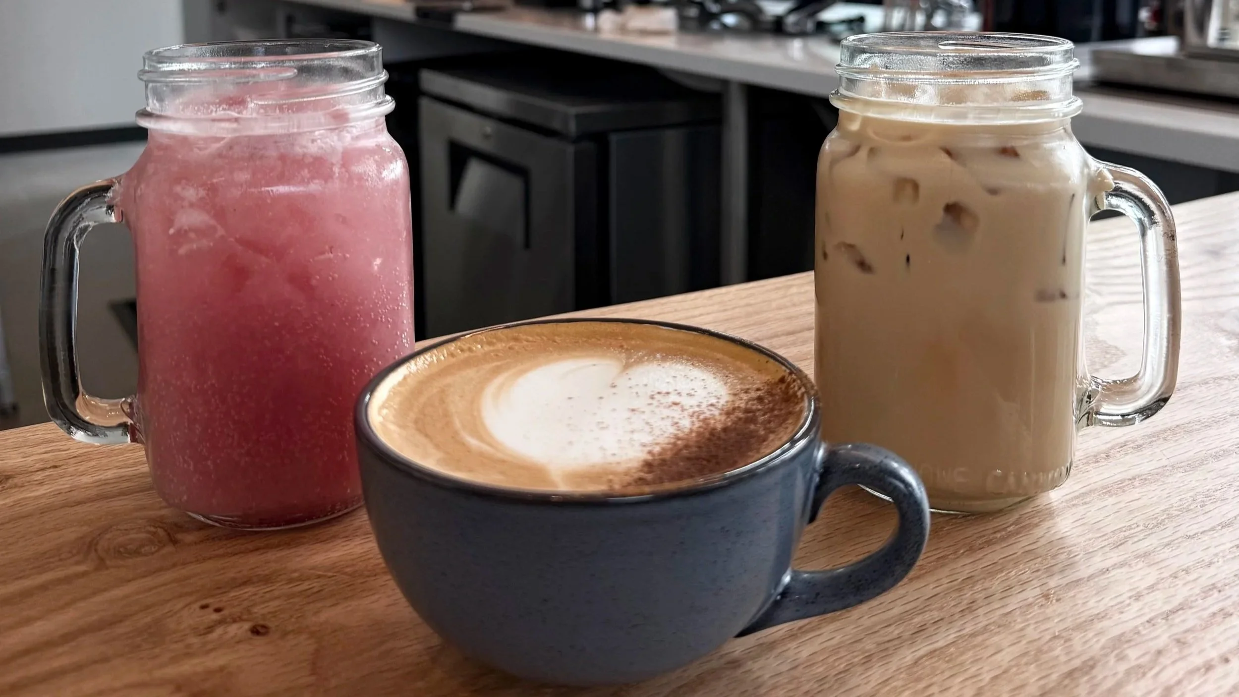 Barista pouring steamed milk into a cup of espresso coffee on a white counter.