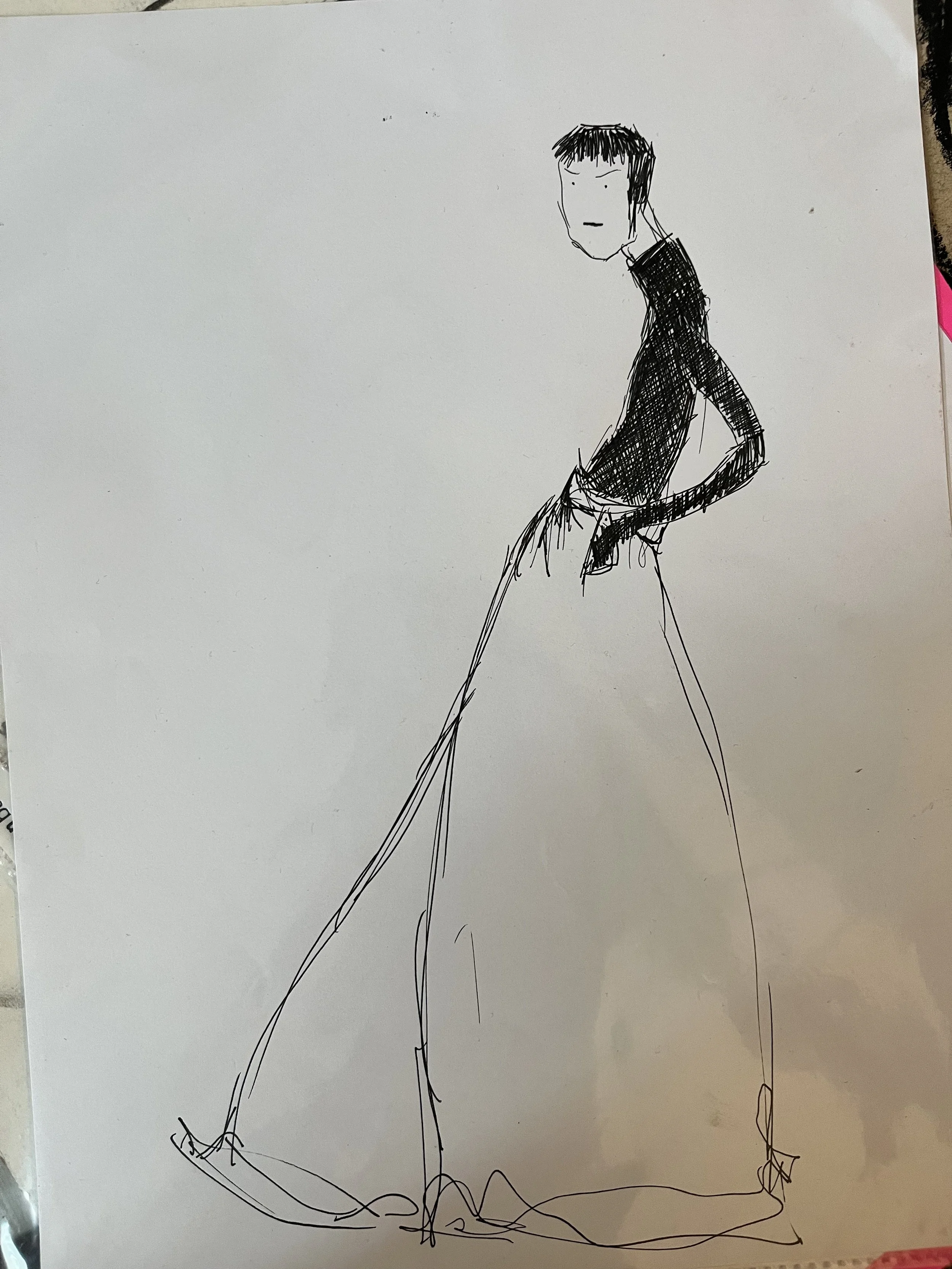 A simple sketch of a tall person standing with one hand in their pocket, wearing a black shirt and a long skirt or pants, with short hair and a neutral expression.