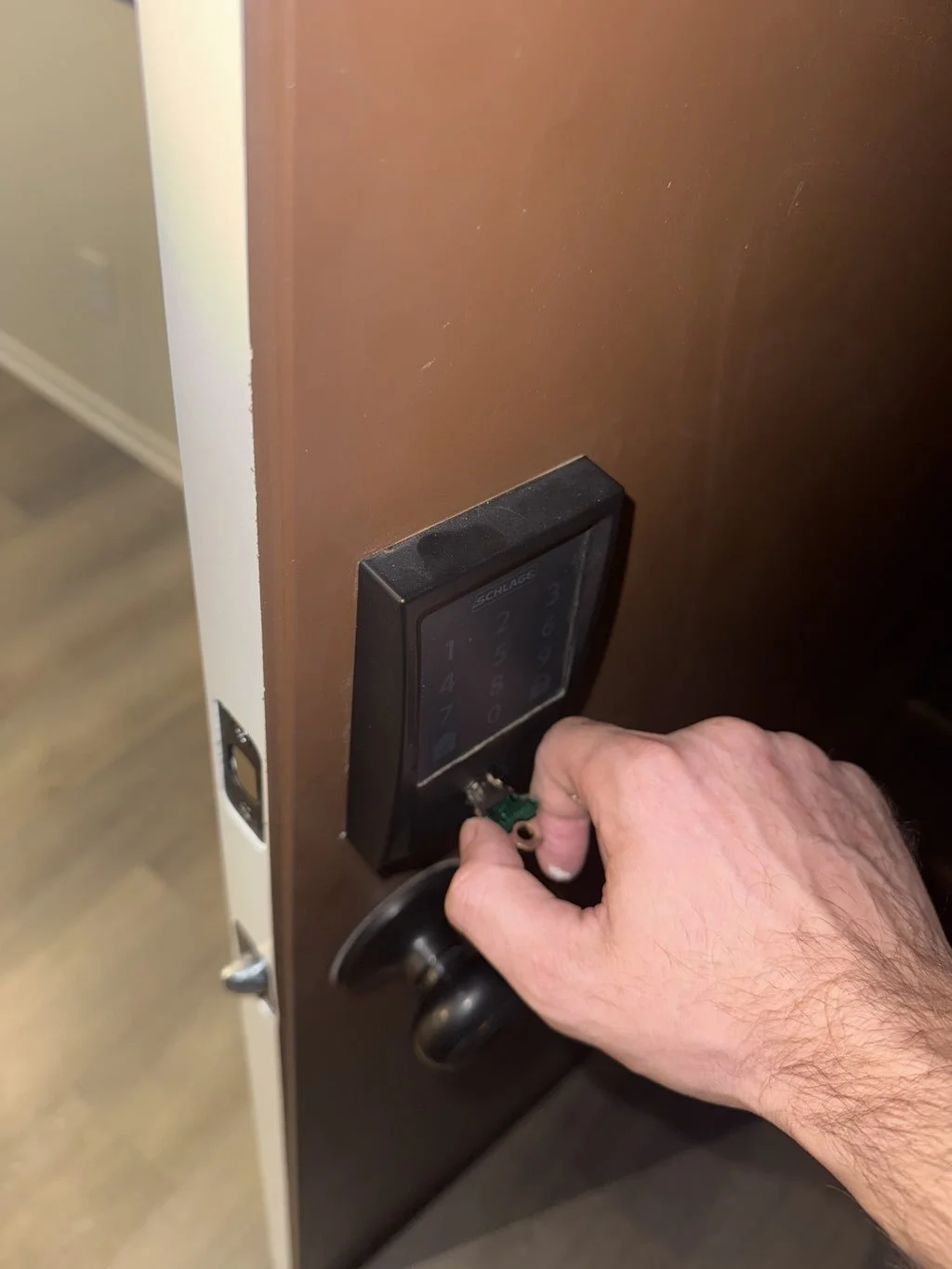 Person's hand removing the electronic lock from a wooden door.