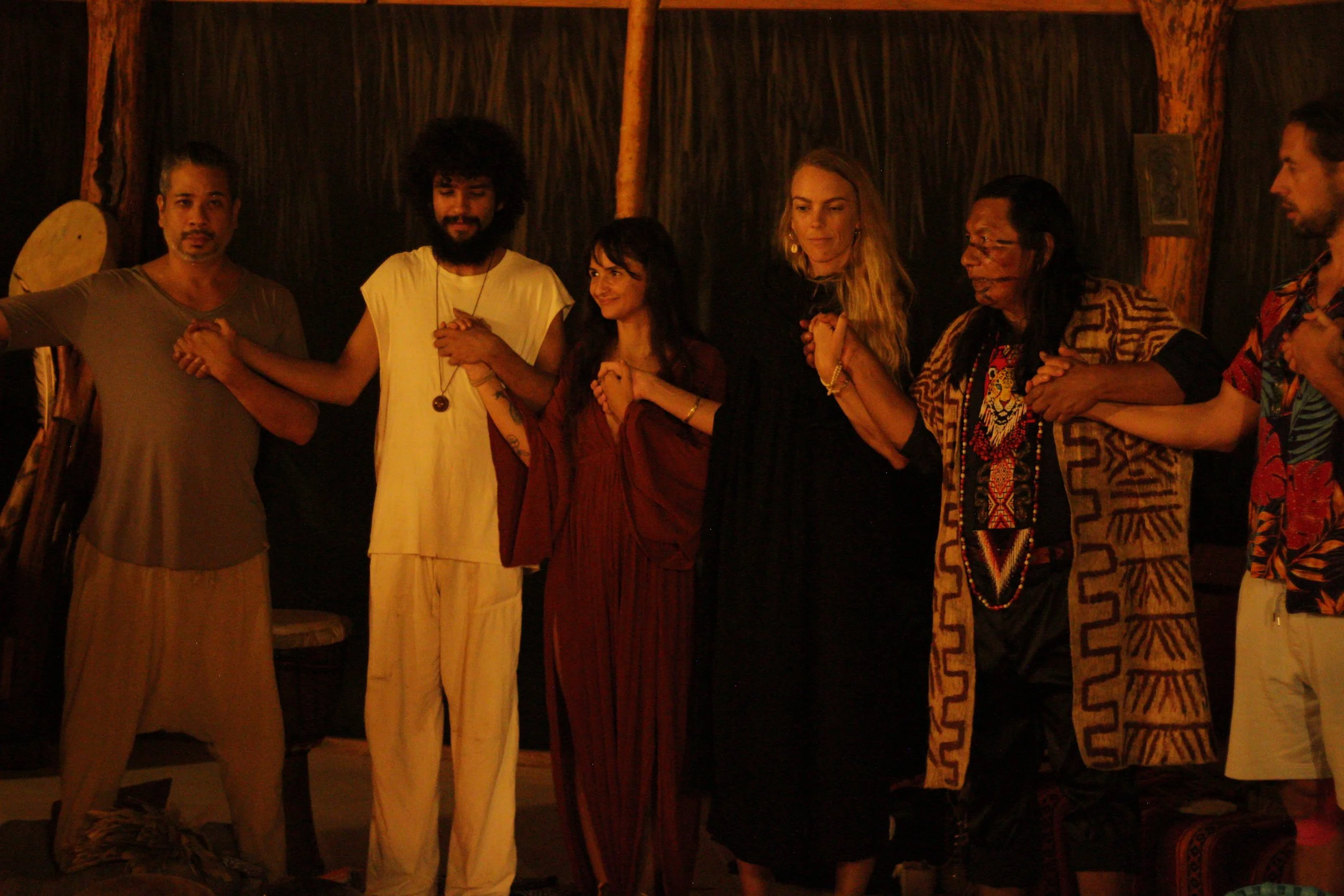 Group of people standing side by side, holding hands, in a dimly lit indoor setting with wooden background.
