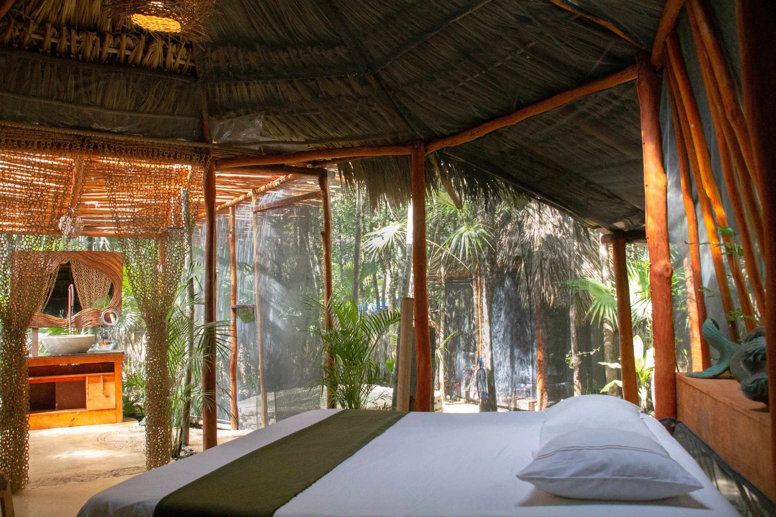 A cozy, rustic bedroom in a tropical setting with natural wood and thatch accents, surrounded by lush greenery and open to the outdoors.