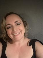 A woman smiling with blonde hair, wearing a black top, against a neutral background.