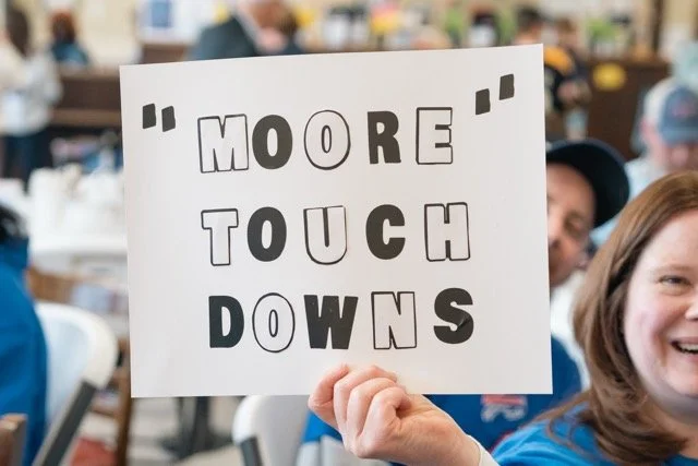 Person holding a sign that says "More Touchdowns" in a crowd at an event or gathering.