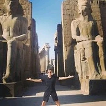 Person standing with arms outstretched between ancient Egyptian statues.