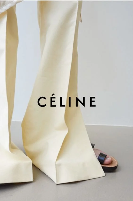 Close-up of cream-colored wide-leg pants and black sandals with gold embellishments, with the Céline logo across the picture.