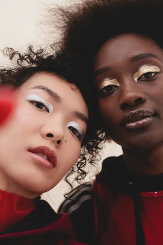 Two women with bold eye makeup taking a close-up selfie together.
