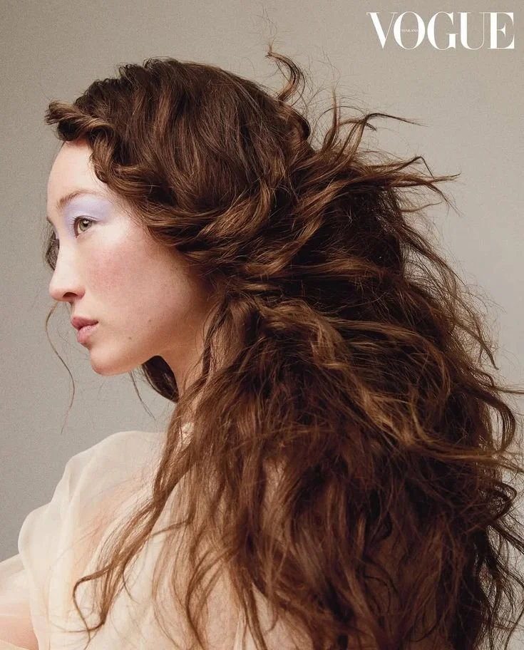 Vogue magazine cover featuring a woman with voluminous, wavy auburn hair, wearing a light-colored top, against a plain background.