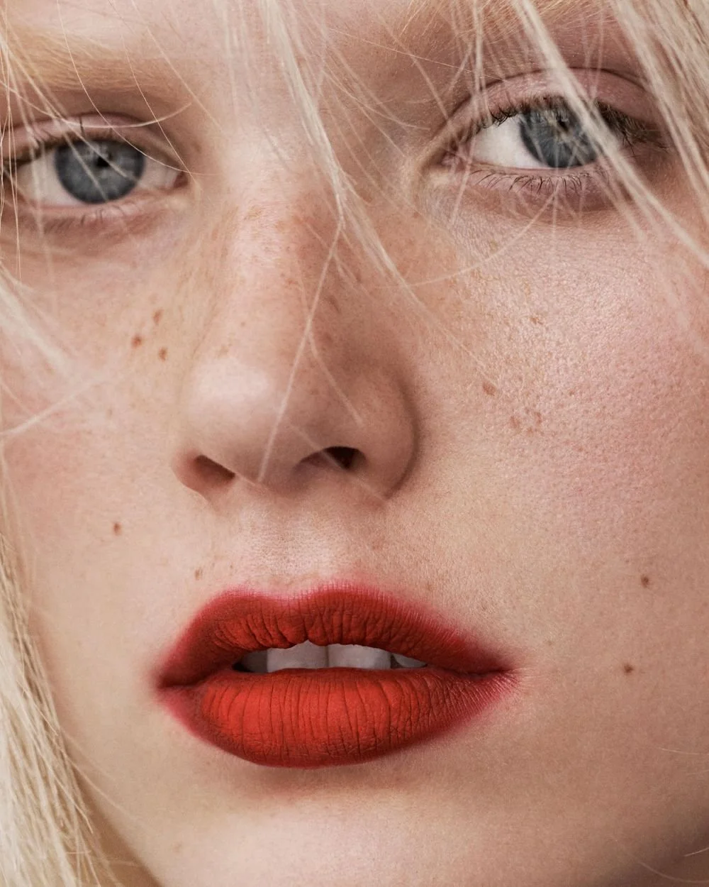 Close-up of a woman's face showing her blue eyes, freckles, and orange lipstick.