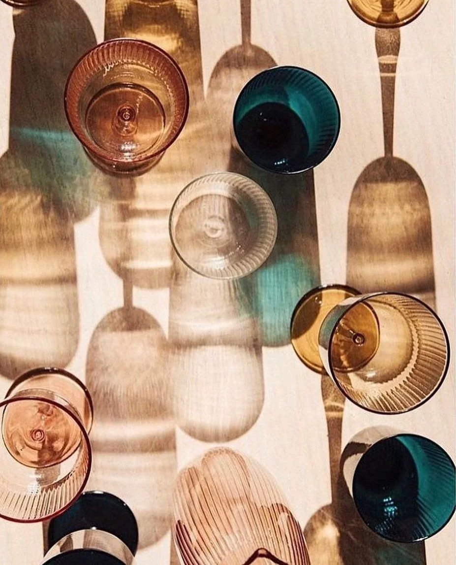 Top-down view of colorful glassware casting intricate shadows on a white surface.