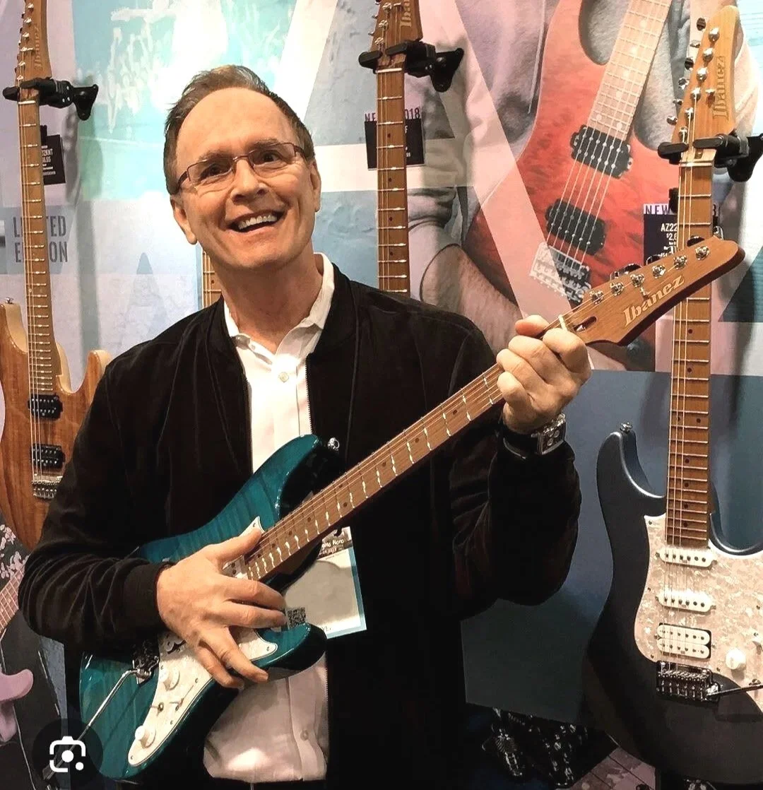 Kim Andrews holding a guitar at his music shop in Newport Beach
