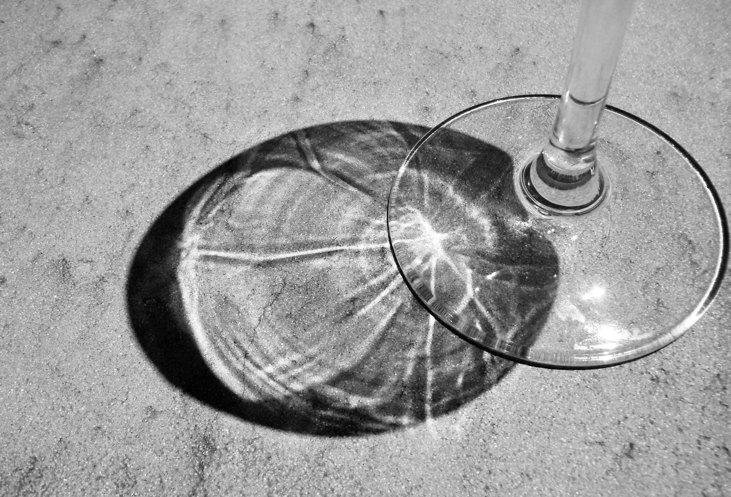 A wine glass on a textured surface is casting a shadow that creates an intricate starburst pattern on the ground.