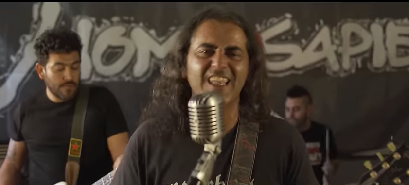 Three musicians performing on a stage with a graffiti-style backdrop, one singing into a vintage microphone.