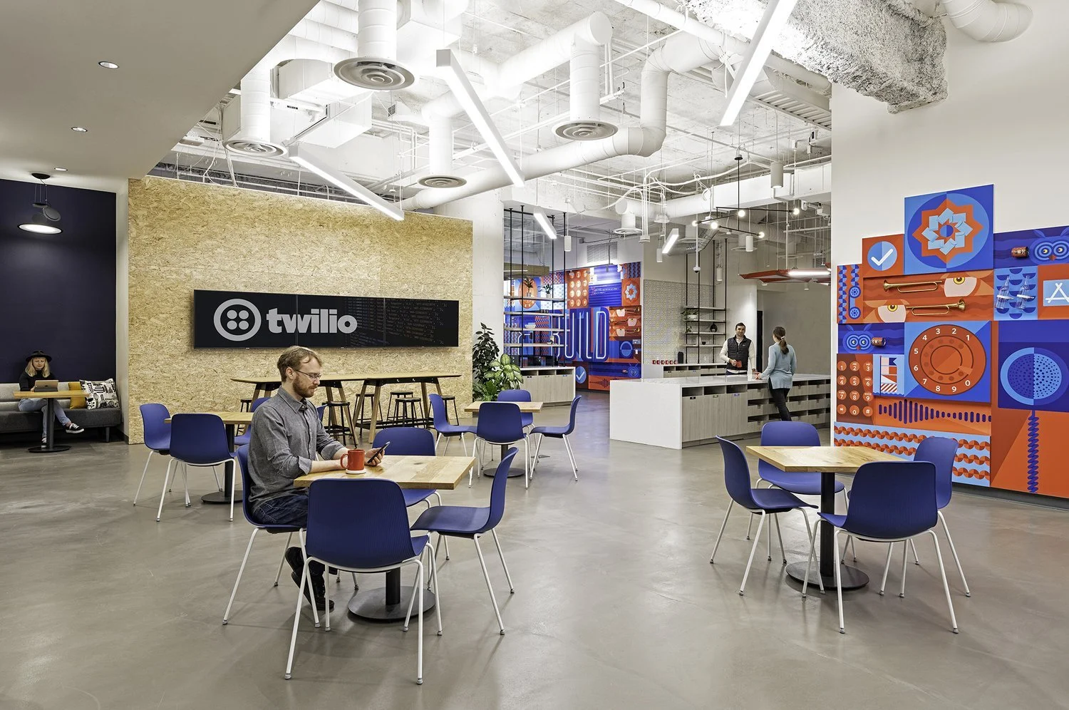 Modern coworking space with seating, a reception area, a colorful mural, and the Twilio logo on a wall.