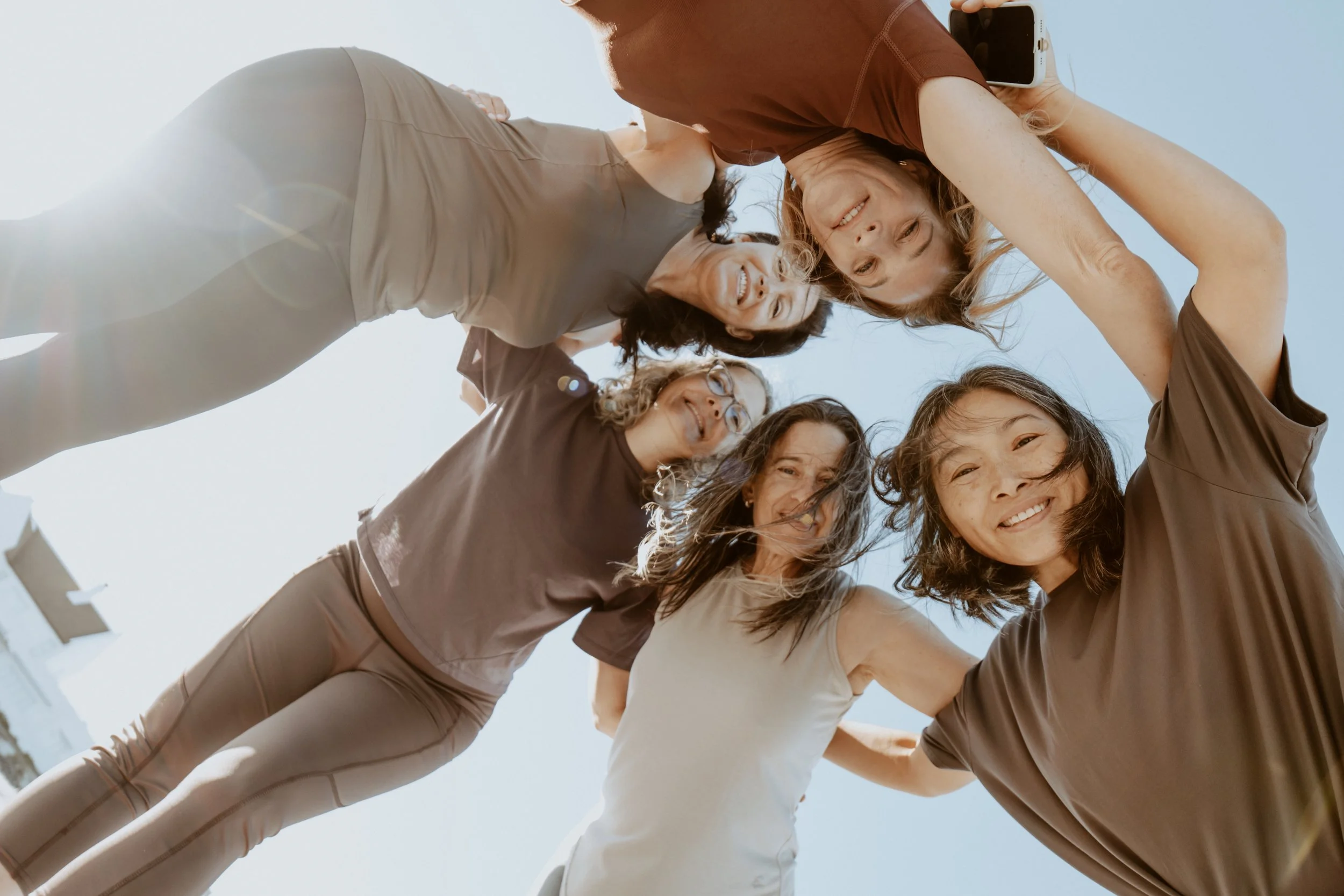 A group of smiling women in atheltic clothing in a circle looking down towards the camera from overhead