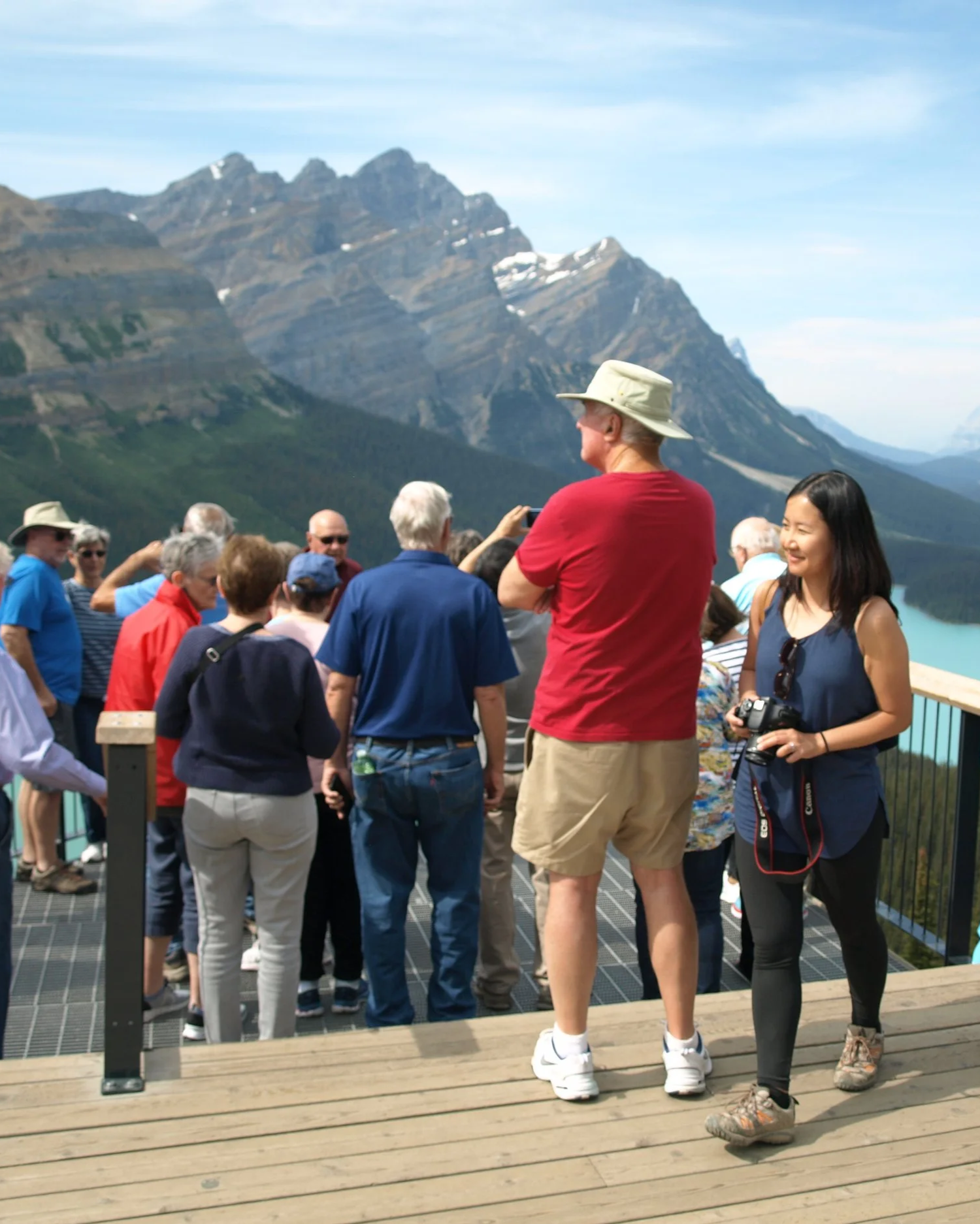 Tourists gathering on a lookout platform at a scenic mountain location, with a lake and rugged mountains in the background.