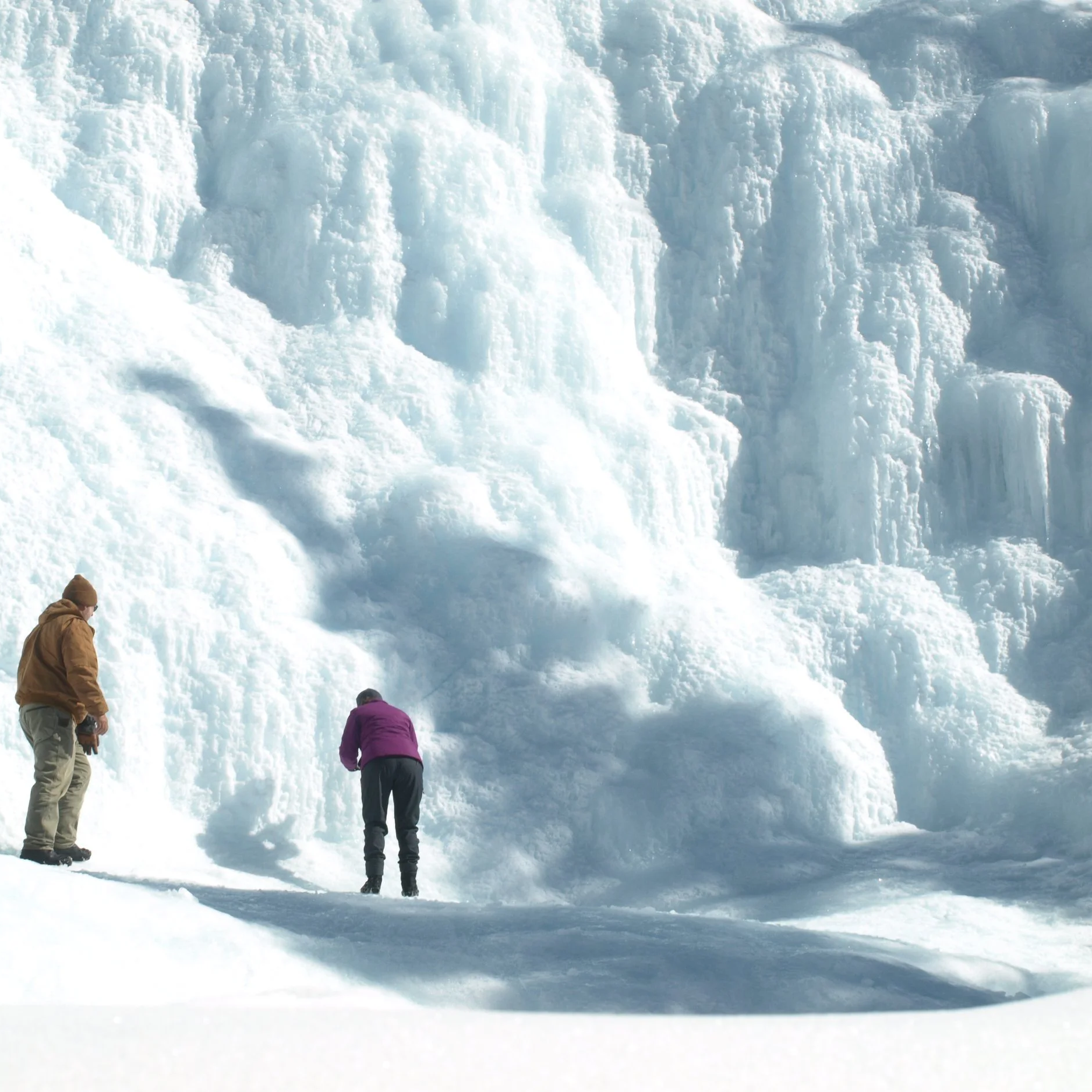 Two people standing near a large glacier with ice formations.