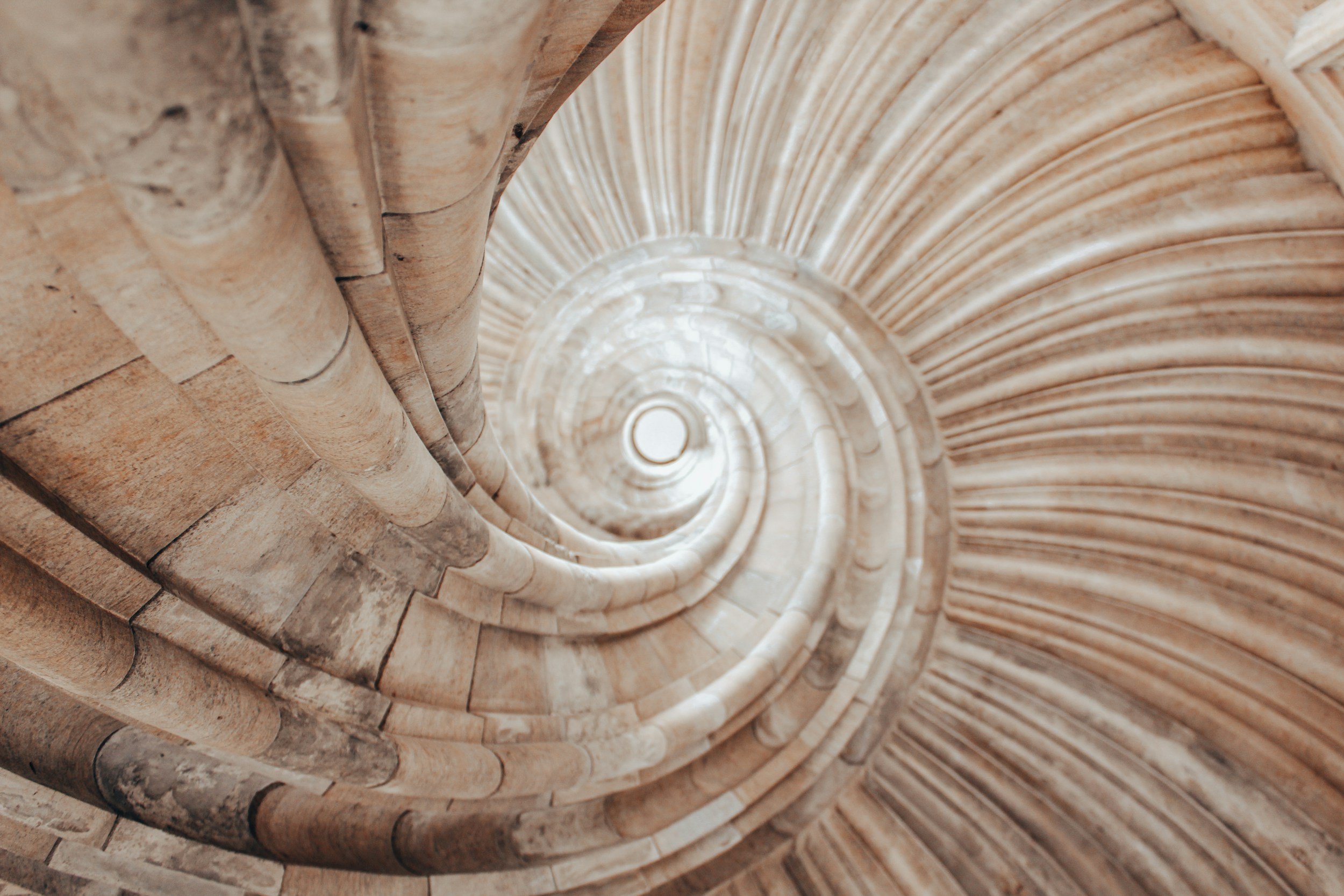 Looking up a spiral stone staircase with circular walls and steps going to the top.