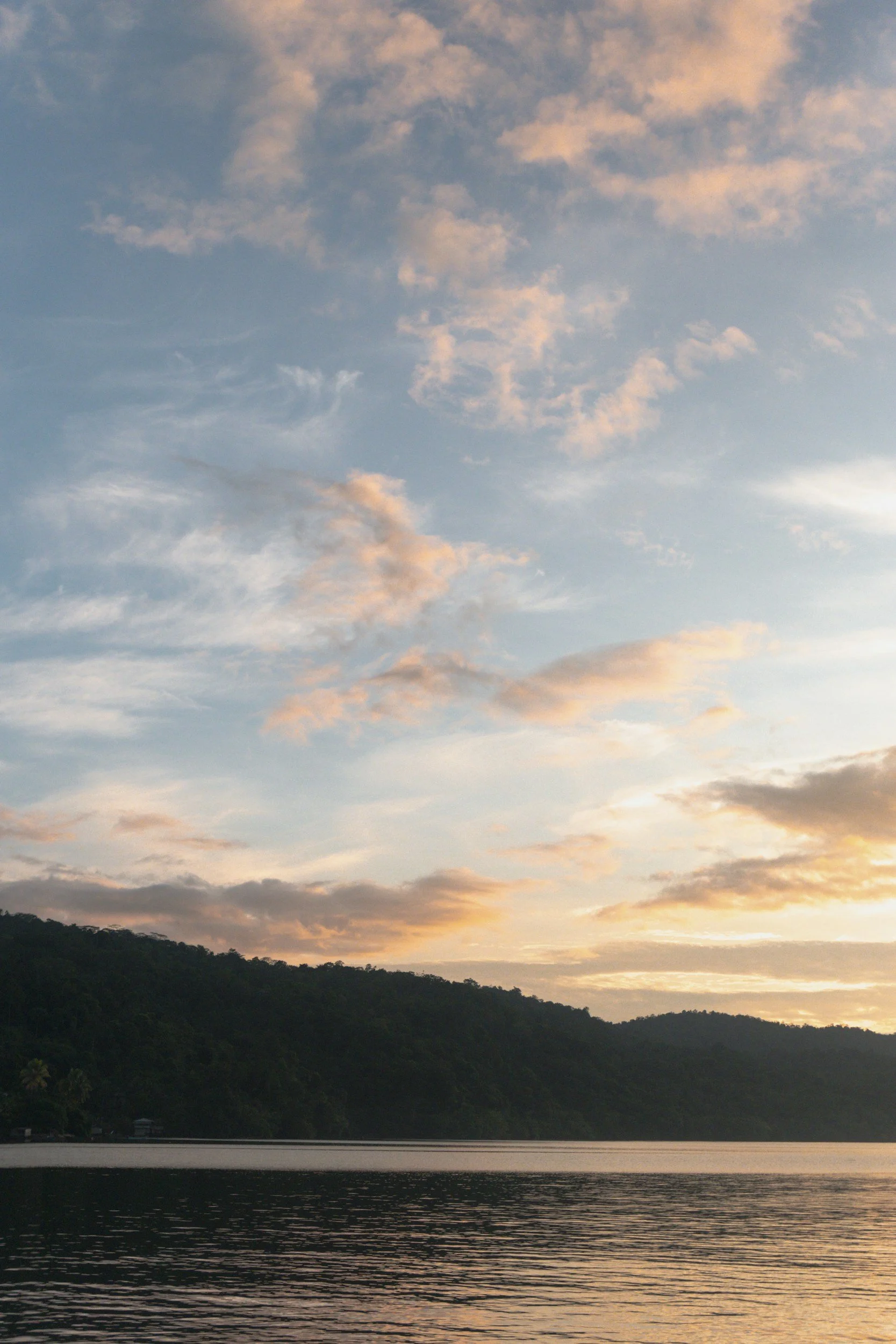 Sunset over a lake with silhouetted hills and a cloudy sky.