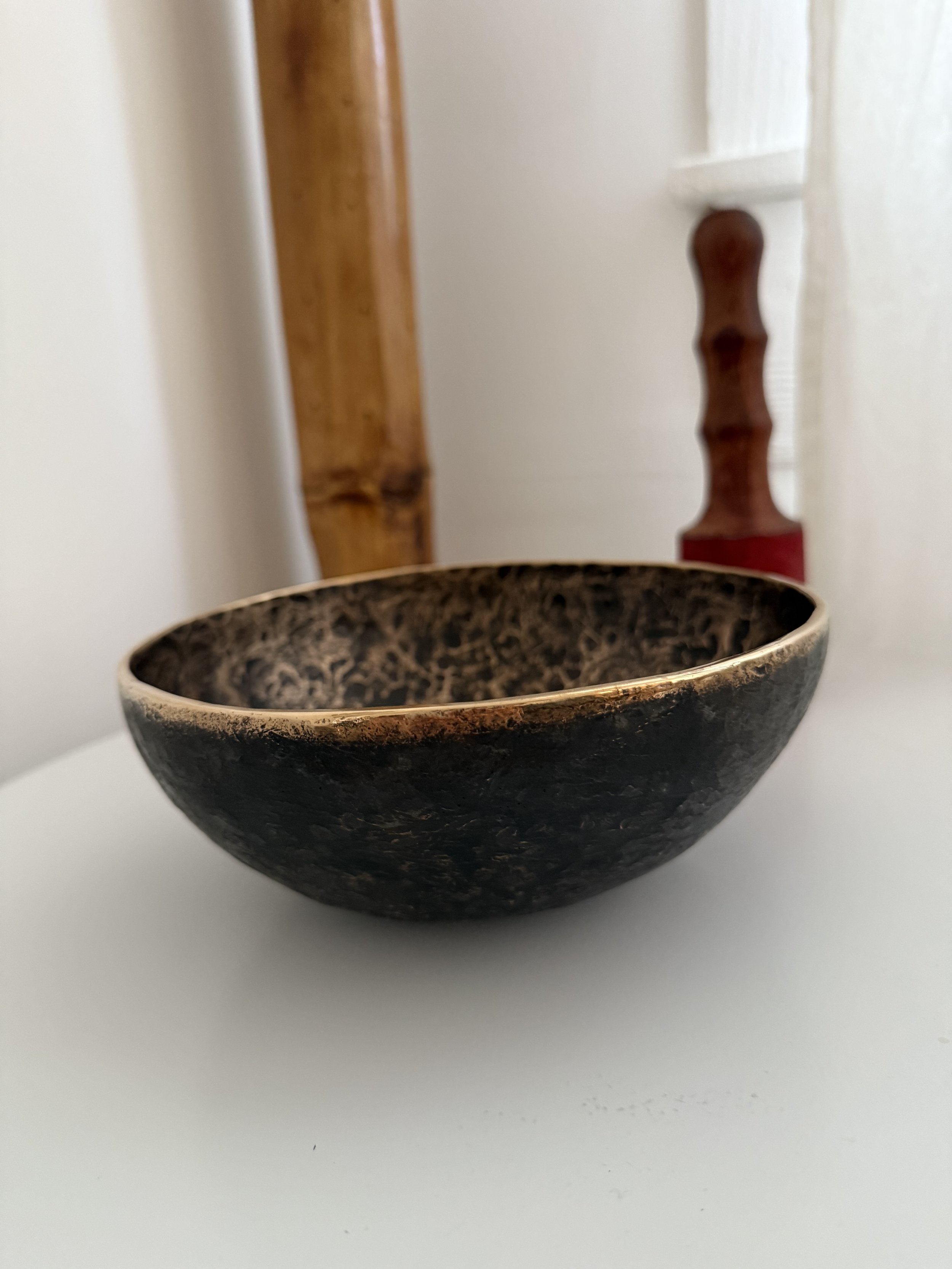 Black and gold decorative bowl on a white surface with a wooden object and red-handled tool in the background.