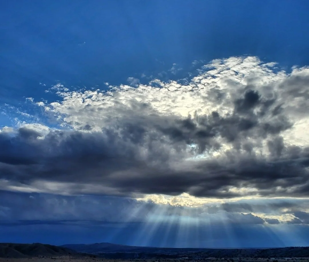Sun rays breaking through cloudy sky over a flat landscape.