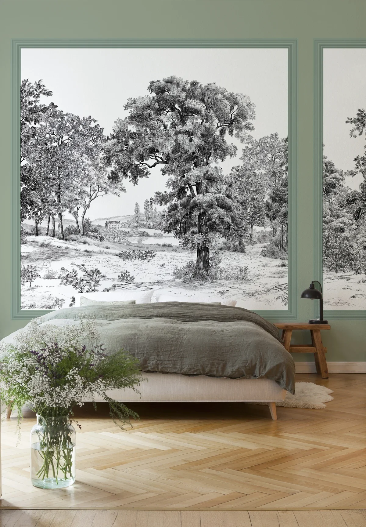 Bedroom with green walls, large window mural of black and white trees and landscape, bed with gray linens, wooden nightstand with black lamp, glass vase with white and purple flowers on wooden floor near bed.
