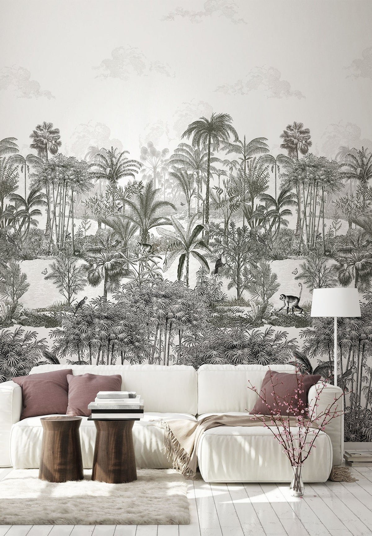Living room with white sofa, pink and purple pillows, wooden side tables, a beige throw blanket, a white shag rug, a white floor lamp, and a wall with black-and-white jungle-themed mural featuring tropical trees, plants, birds, and a monkey.