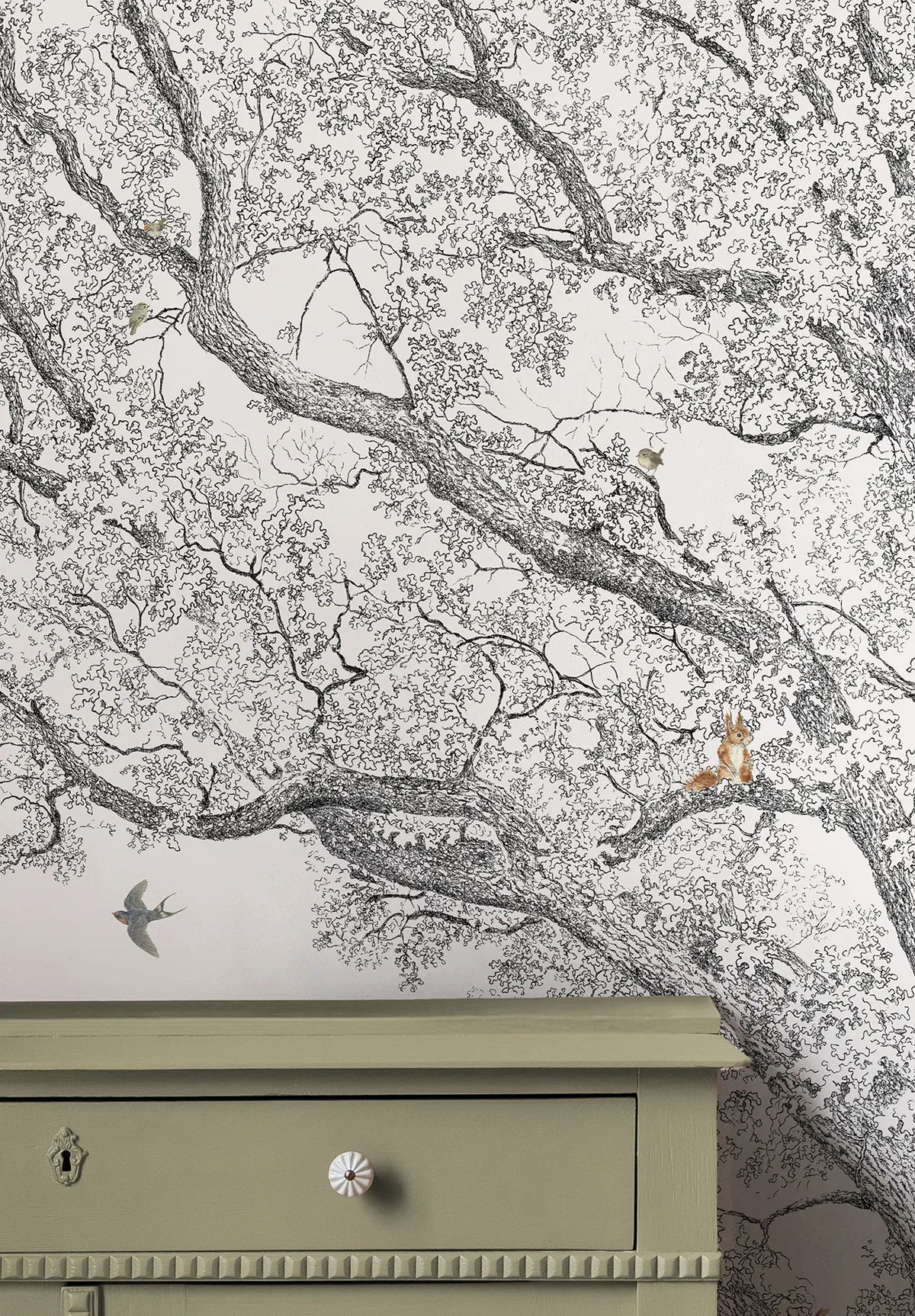 Decorative wall with a tree branch design and small bird and squirrel illustrations, with part of a light green dresser visible at the bottom.