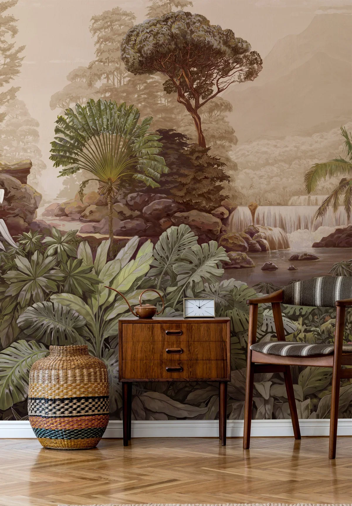 A decorative wall mural depicting a lush tropical rainforest with waterfalls and dense greenery. In front of the mural, there is a wooden side table with a clock and a teapot, a woven basket, and a vintage-style chair with a patterned cushion.