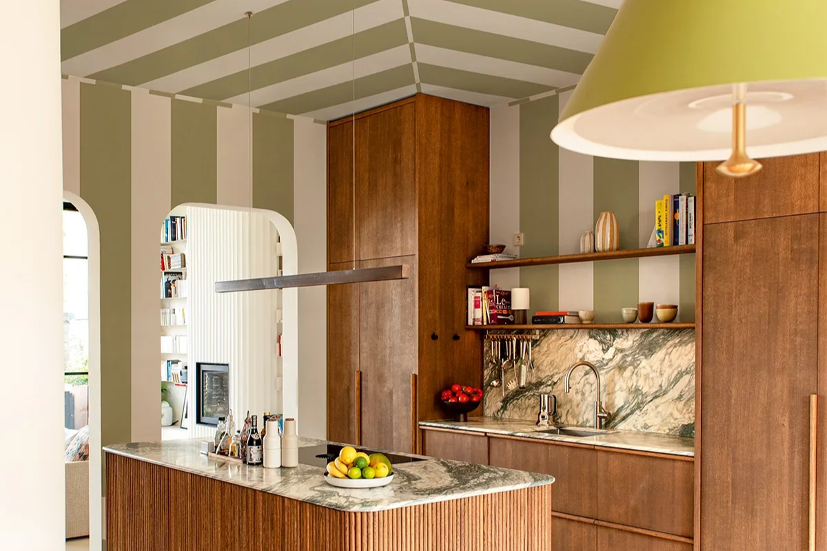Modern kitchen with wooden cabinets, a marble countertop, and open shelving. A bowl of lemons and limes is on the island, and a hanging pendant light is visible.